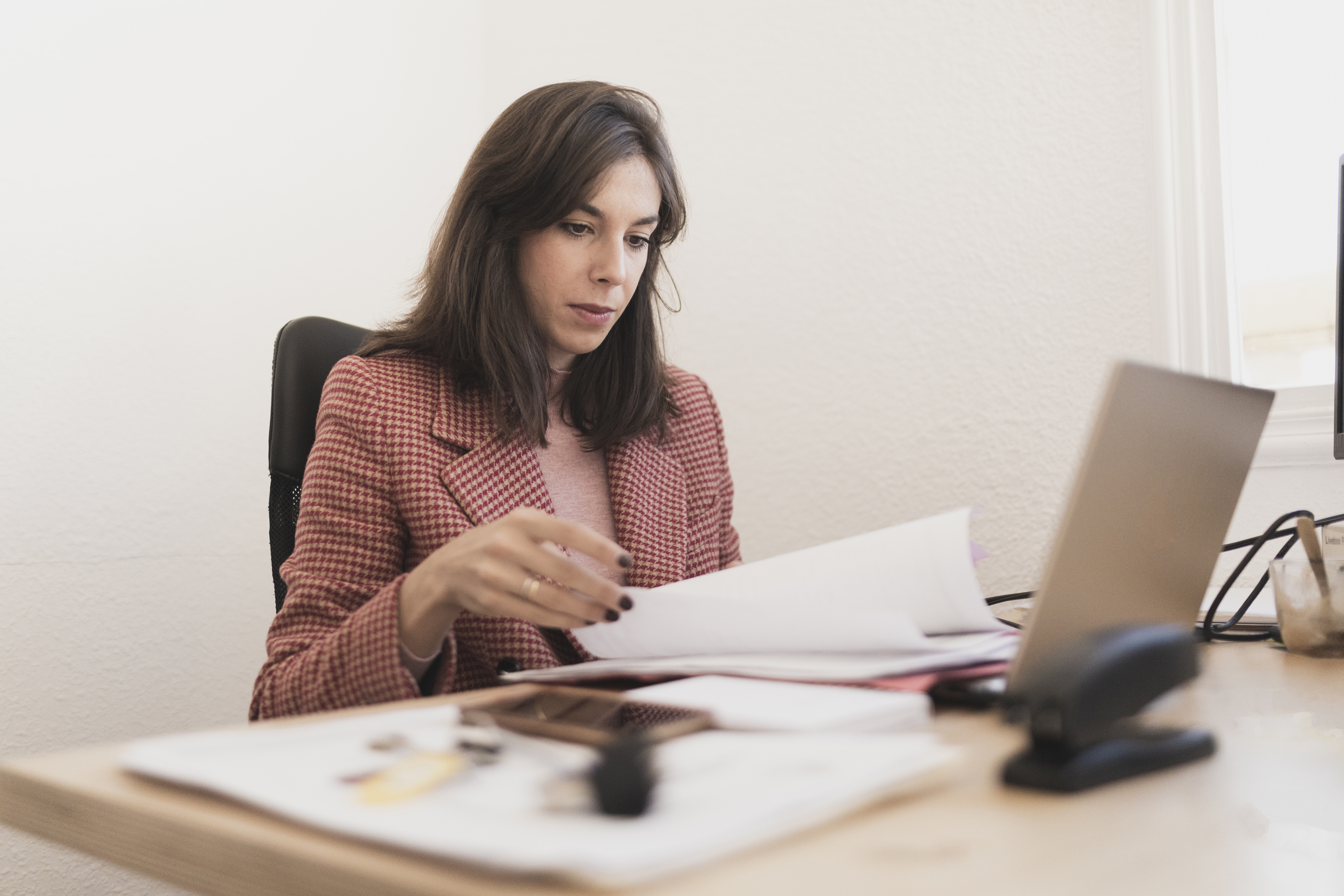 Serious woman with documents near laptop at workplace